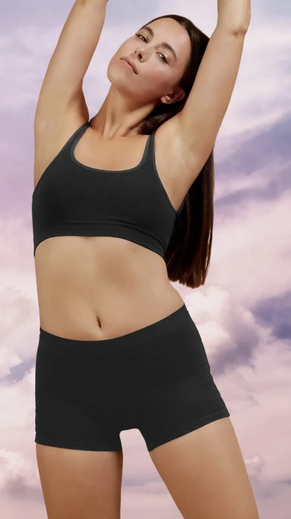 Czarne majtki menstruacyjne Fluxies Sleep Short na szczęśliwej kobiecie w czarnym topie na fioletowym tle, widok z przodu