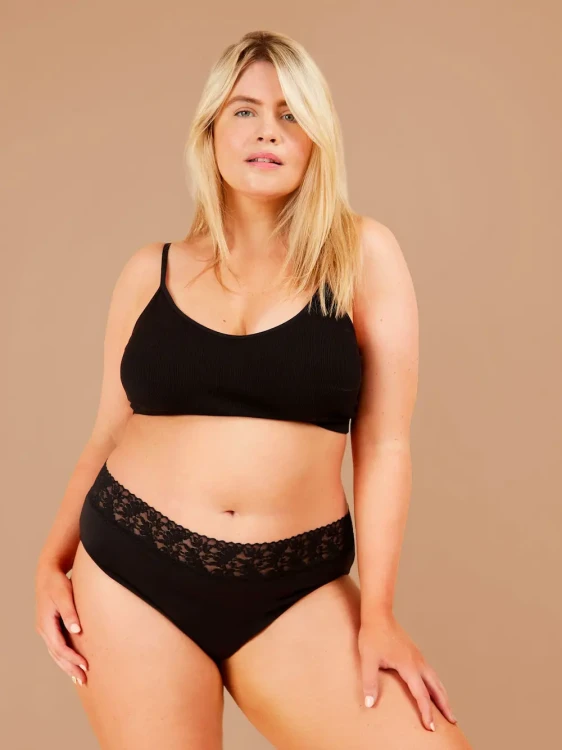 Czarne majtki menstruacyjne Fluxies Bikini z koronką w pasie na modelce plus size, widok z przodu
