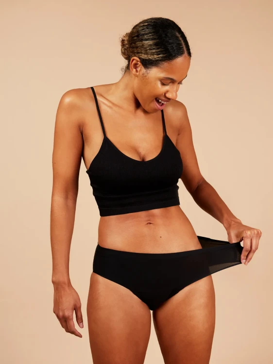 Modelka w czarnych majtkach Fluxies NuStretch rozciąga materiał z uśmiechem